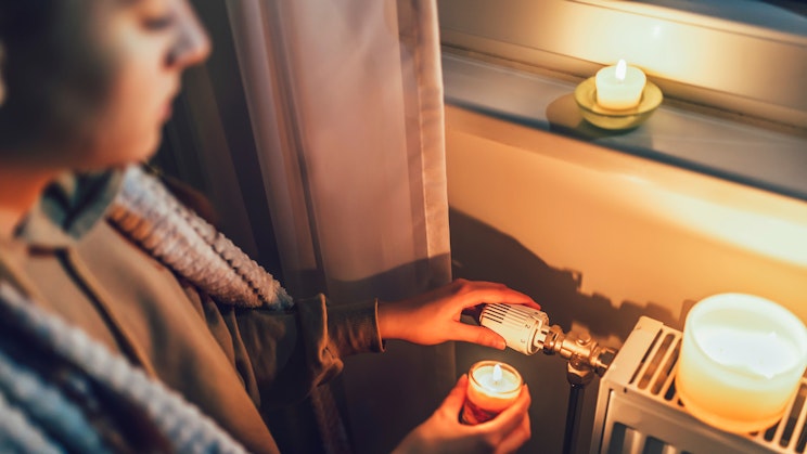 Ihminen säätämässä patterin lämpötilaa kynttilän valossa.