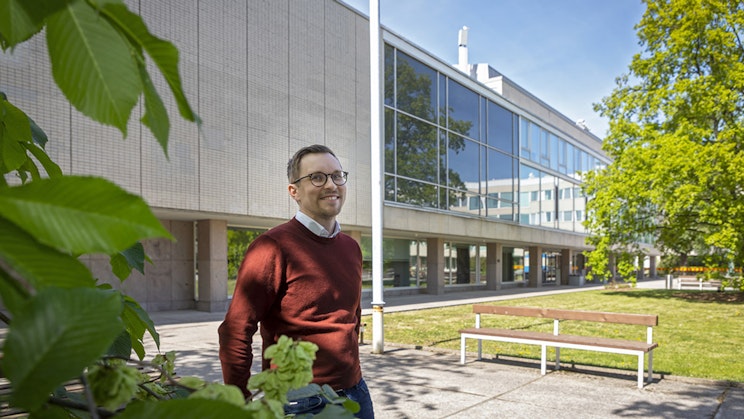 Miesoletettu seisoo rakennuksen edessä kädet selän takanaan hymyilee suoraan kameraan.