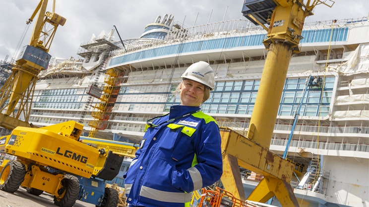 Ihminen seisoo nosturin ja rakenteilla olevan risteilyaluksen edessä.