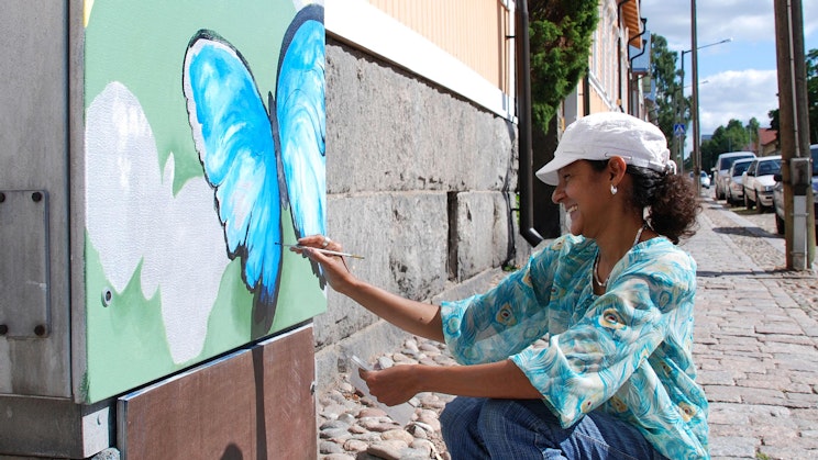 nainen maalaa seinämaalausta rakennuksen kylkeen