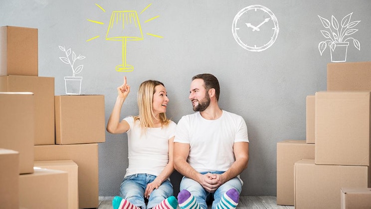 mies ja nainen istuvat lattialla pahvilaatikoiden ympäröimänä