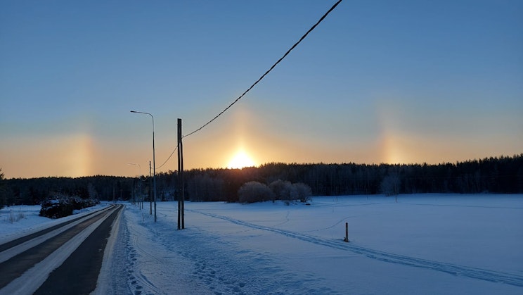 aurinko laskee lumisen tien yli