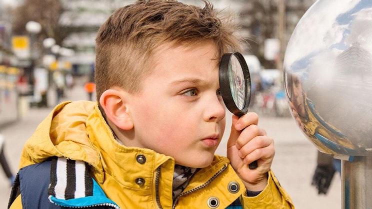 Kuvassa poika katsoo suurennuslasilla kaukolämmön tuuletusputkea