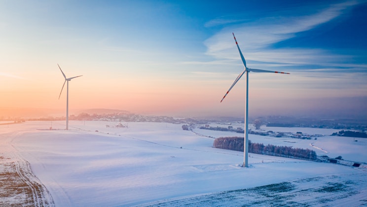 Kuvassa kaksi tuulivoimalaa talvimaisemassa