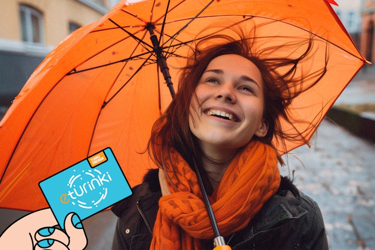 Tuulisessa sadekelissä iloinen tyttö oranssin sateenvarjon kanssa.