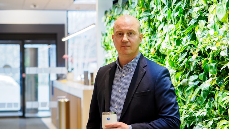 Kuvassa seisoo mies viherseinän edessä, kahvikuppi kädessä