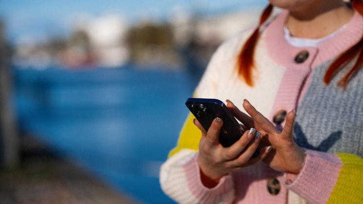 Nainen käyttää kännykkää jokirannassa.