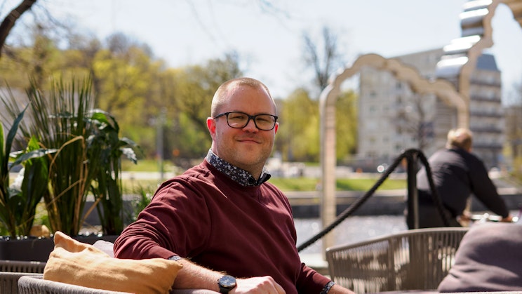 Mies istuu tuolilla ja katsoo kameraan Turun jokirannassa.