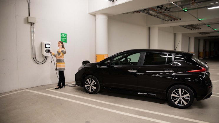 Nainen lataa mustaa sähköautoa