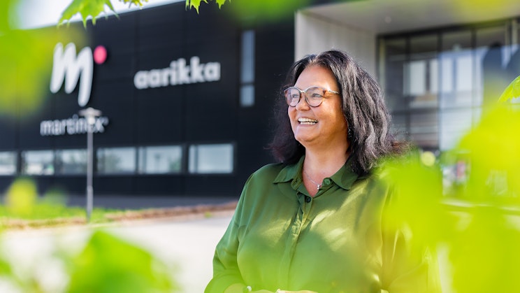 Kuvassa tummatukkainen nainen hymyilee ja kuvaa kehystää vihreät puun lehdet