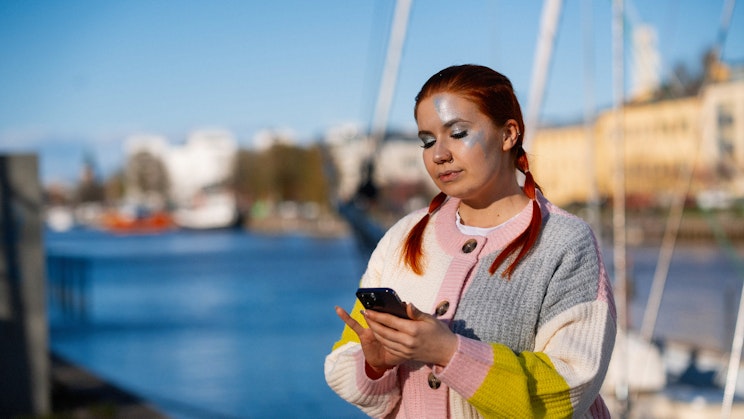 Naisoletettu selaa Aurajoen rannassa puhelinta