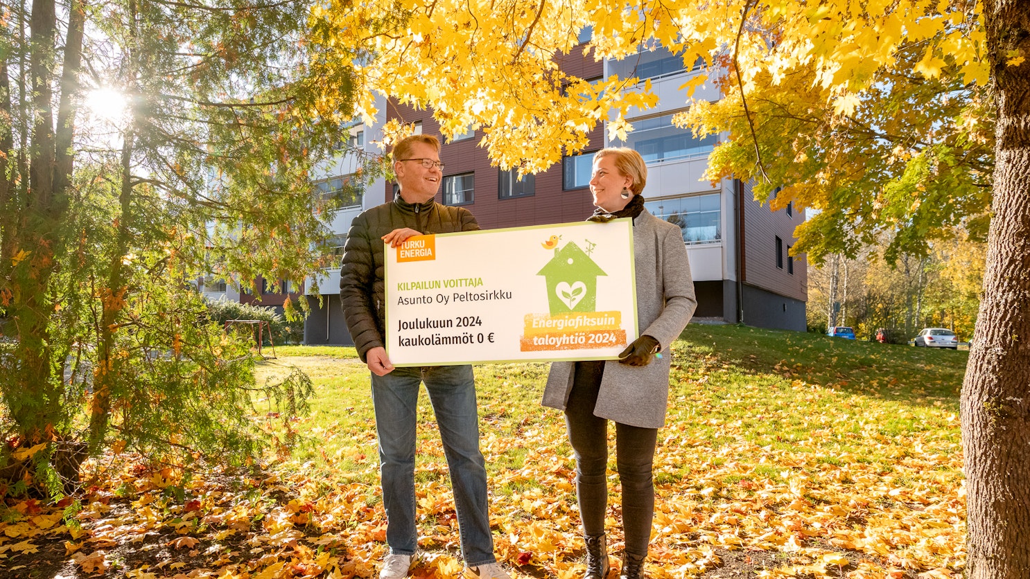 Mikko Paavolainen ja Susanna Tuominen seisovat syksyisessä maisemassa pitelemässä palkintosekkiä.