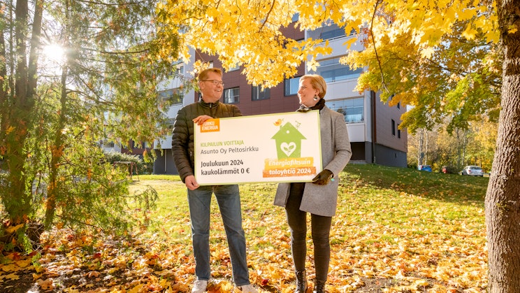 Mies ja nais oletetu seisovat syksyisessä maisemassa pitelemässä palkintosekkiä