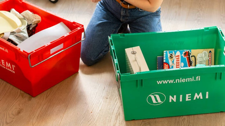 Naisoletettu kahden muuttolaatikon takana lukee kirjan takakantta