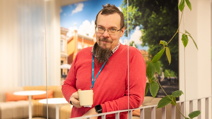 Hymyileväinen Juho Uurasjärvi pitelee kahvikuppia toimistotiloissa.