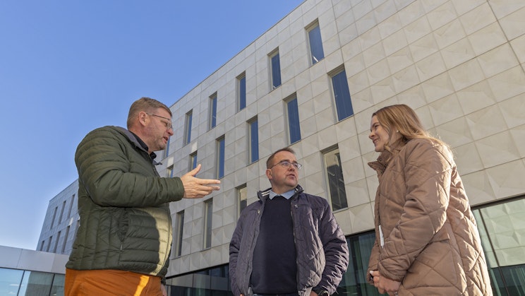 Kolme henkilöä käyvät keskustelua ison rakennuksen edessä