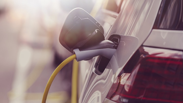 Valkoinen sähköauto latautumassa parkkipaikalla