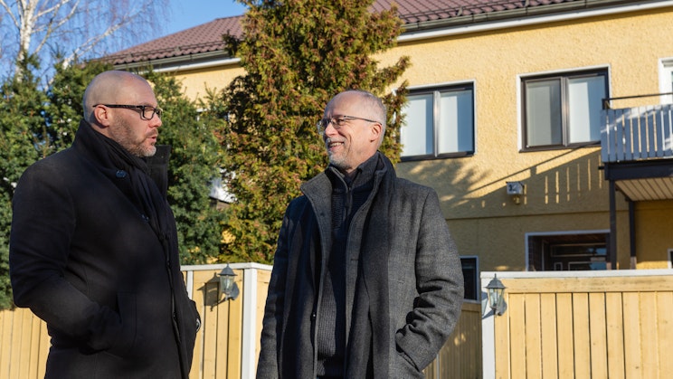 Kaksi miesoletettua keskustelevat keltaisen talon edustalla