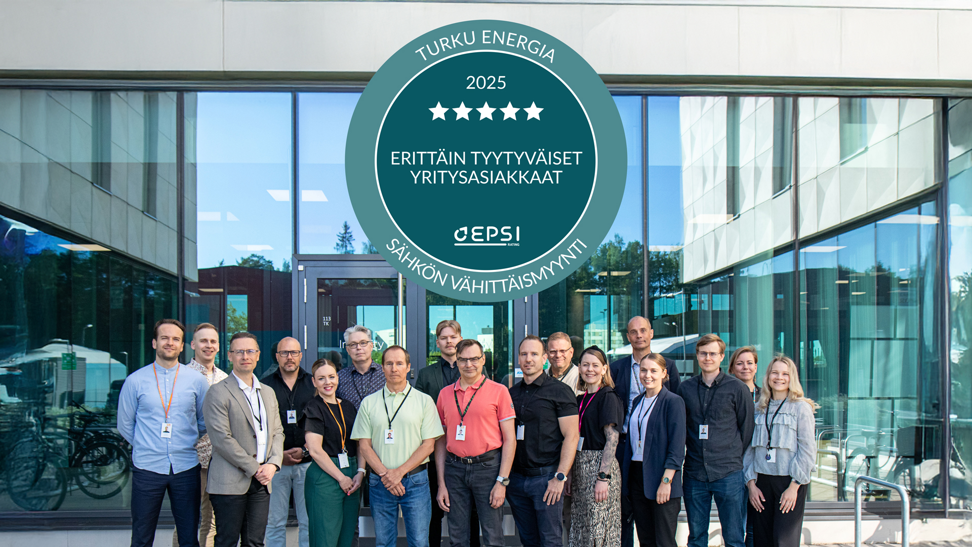 Ryhmä ihmisiä seisoo ulkona modernin lasijulkisivuisen rakennuksen edessä. Kuvan yläosassa on suuri vihreä ympyränmuotoinen merkki, jossa lukee: Turku Energia 2025 – Erittäin tyytyväiset yritysasiakkaat – EPSI – Sähkön vähittäismyynti. Merkissä on myös viisi valkoista tähteä.