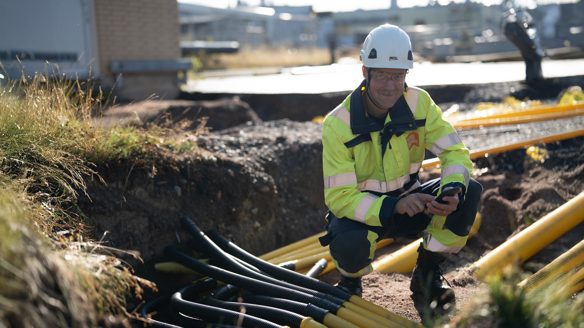 Turku Energia Sähköverkkojen työntekijä työskentelee kaivannossa, jossa on useita keltaisia ja mustia suojaputkia sähkökaapeleille.