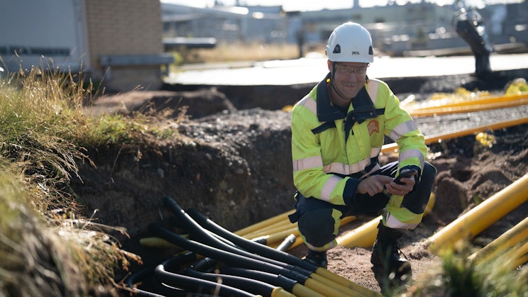 Turku Energia Sähköverkkojen työntekijä työskentelee kaivannossa, jossa on useita keltaisia ja mustia suojaputkia sähkökaapeleille.