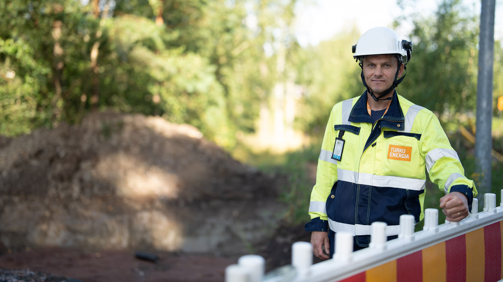 Turku Energia Sähköverkkojen työntekijä seisoo työmaa-alueella puna-keltaisen aidan vieressä.