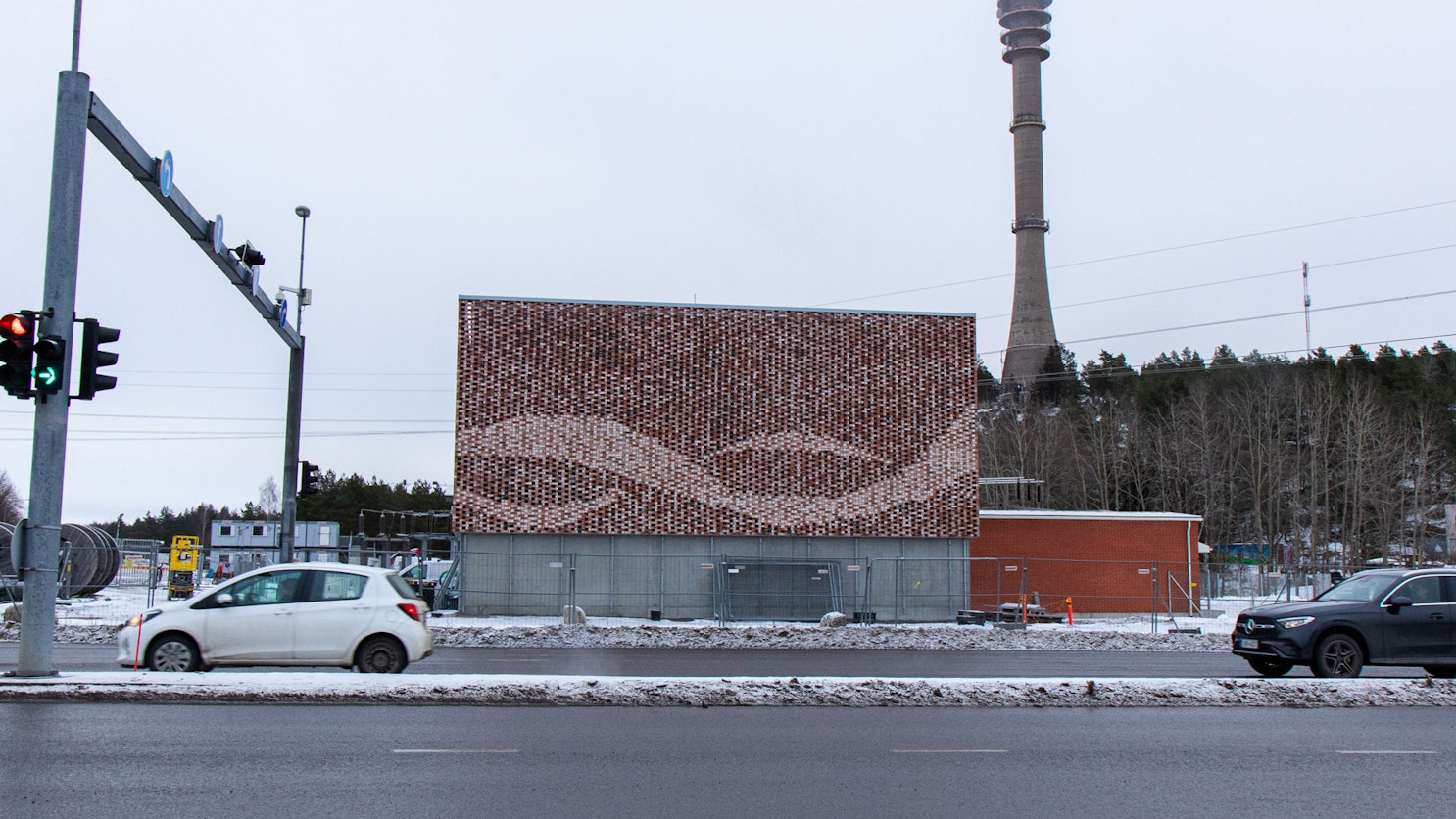 Valokuva Pääskyvuoren sähkökattilarakennuksesta talvisessa maisemassa. Rakennuksen julkisivua koristaa punasävyinen tiilimosaiikki, jossa on aaltoileva kuvio.
