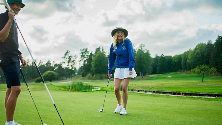 Kaksi nauravaista golf-pelaajaa viheriöllä.