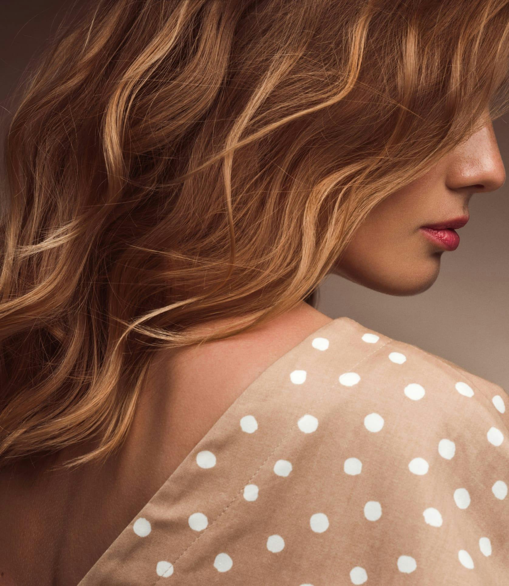 Side profile of a woman with long red curly hair wearing a polka dot top
