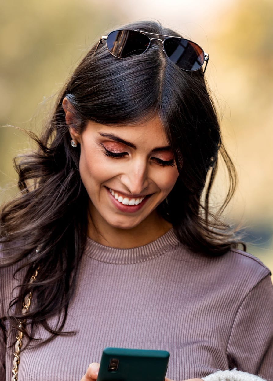 Woman with long dark curly hair smiling while looking at her phone