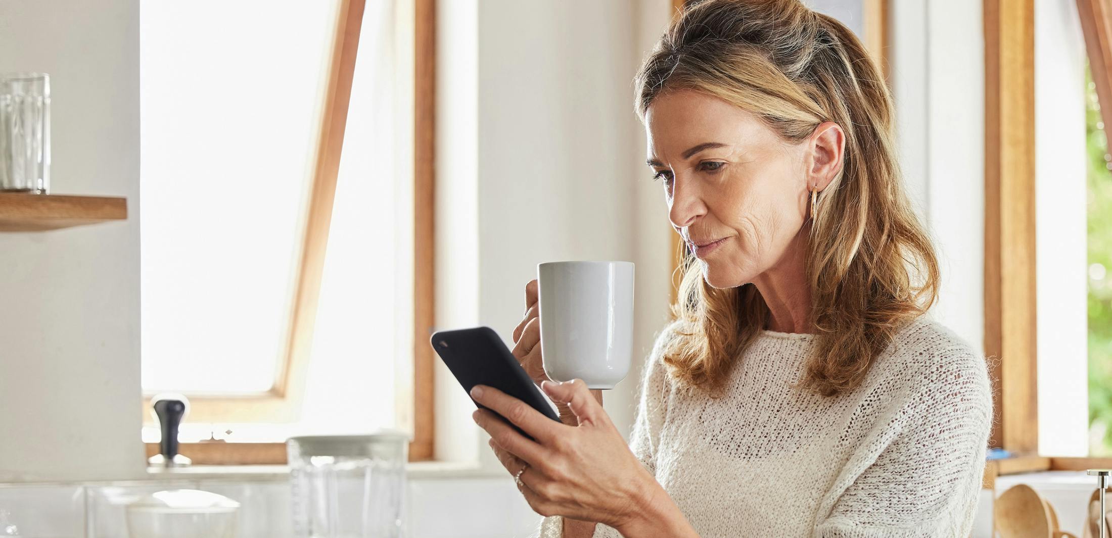 woman holding a cup and looking at her phone