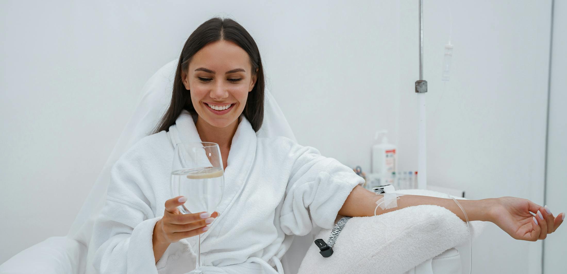 Woman receiving IV therapy while holding a glass of water