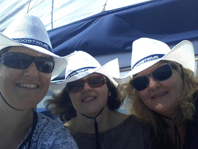Three people wearing white sun hats and sunglasses smiling outdoors, with part of a boat canopy visible in the background.