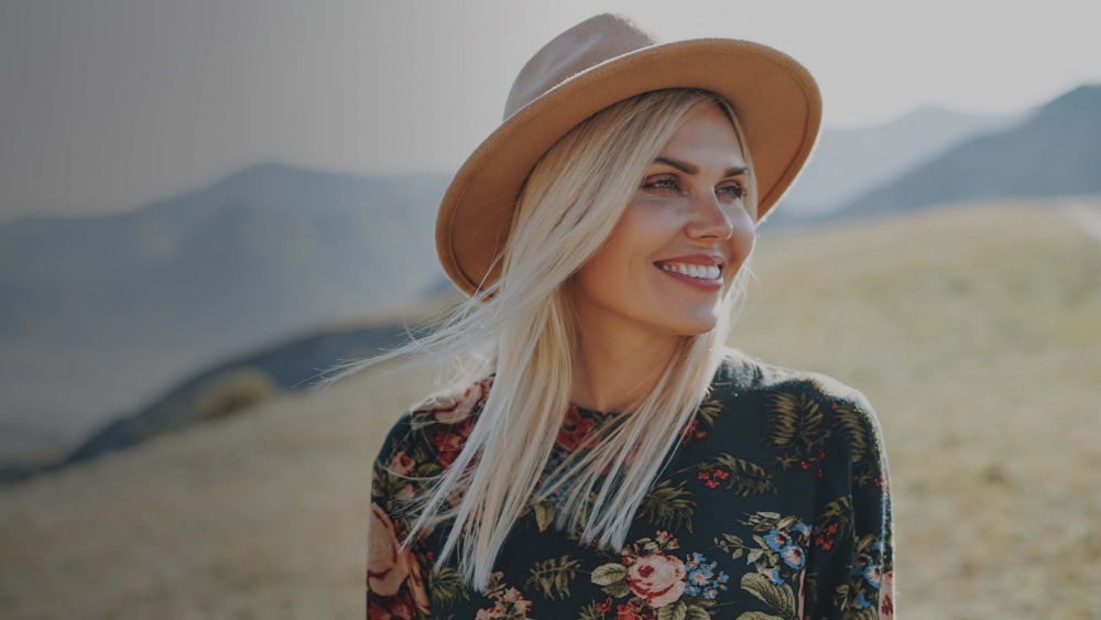 Woman smiling and wearing a hat in the mountains.
