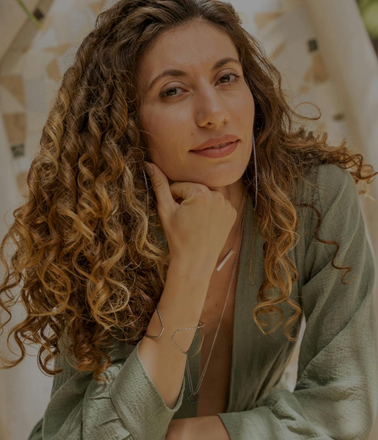 Woman with curly hair resting her chin on her hand.