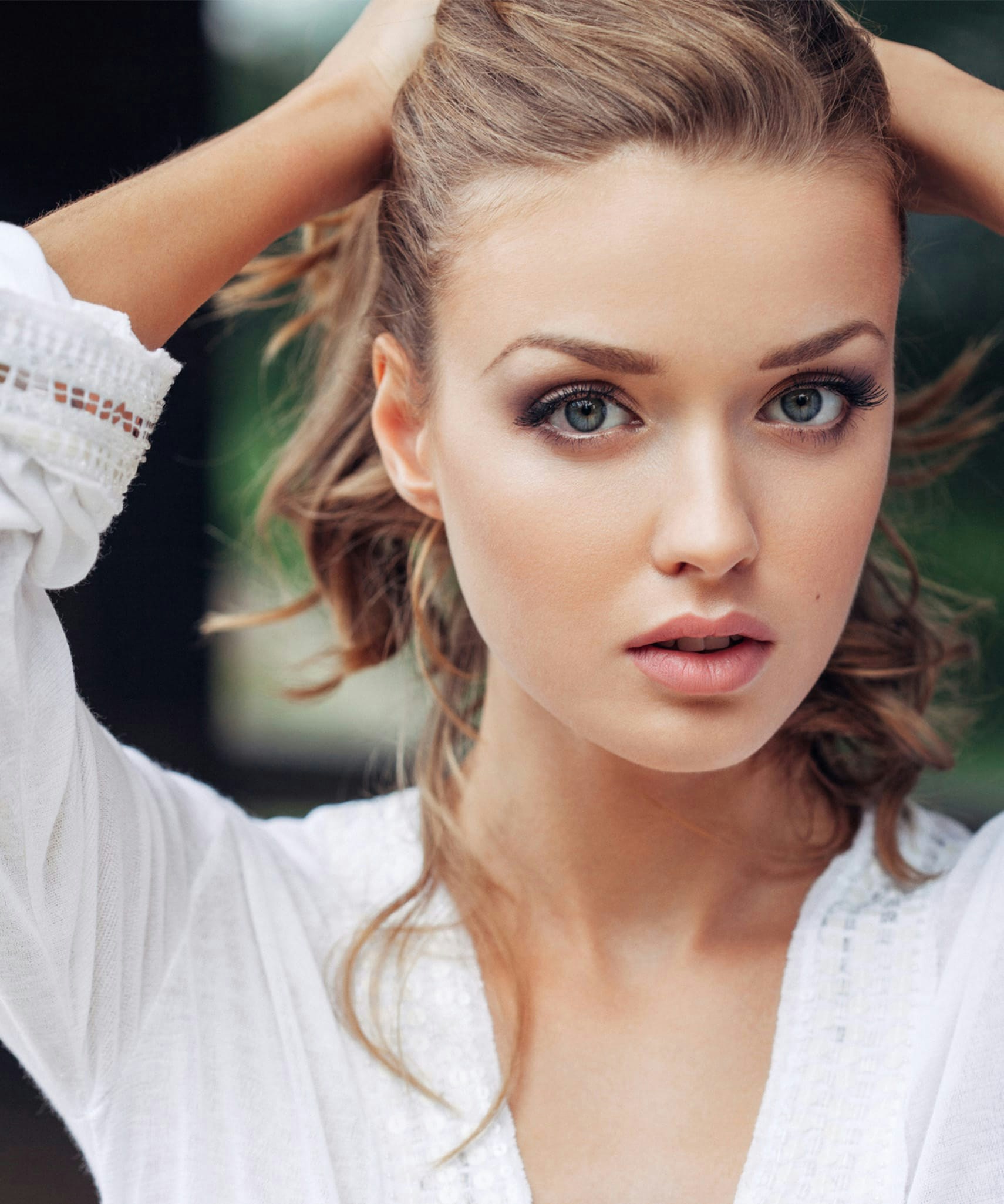 Woman with her hands on her hair looking at the camera.