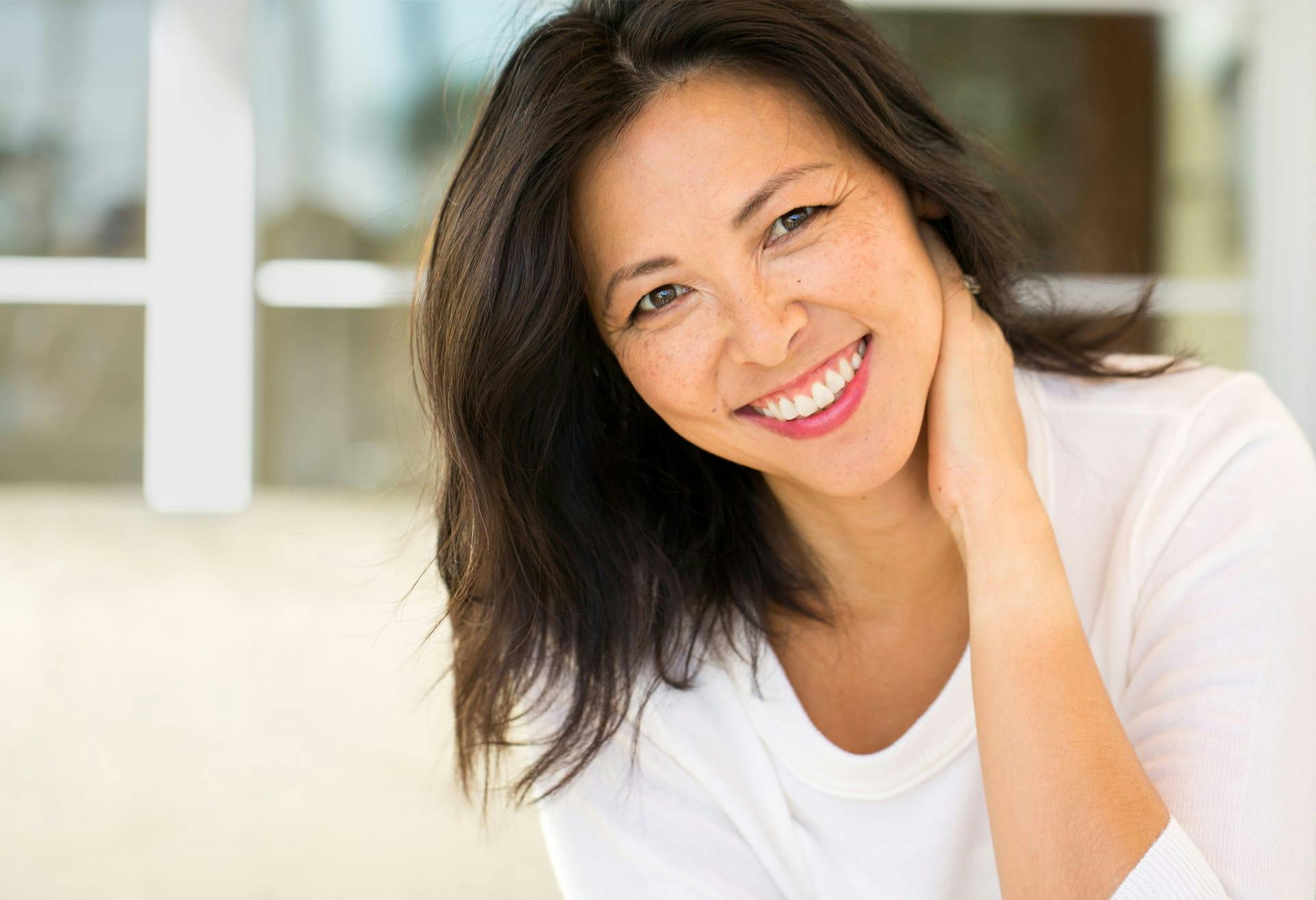 Smiling woman wearing white shirt with hand on back of neck.