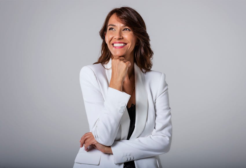Smiling woman in white blazer with hand under chin.