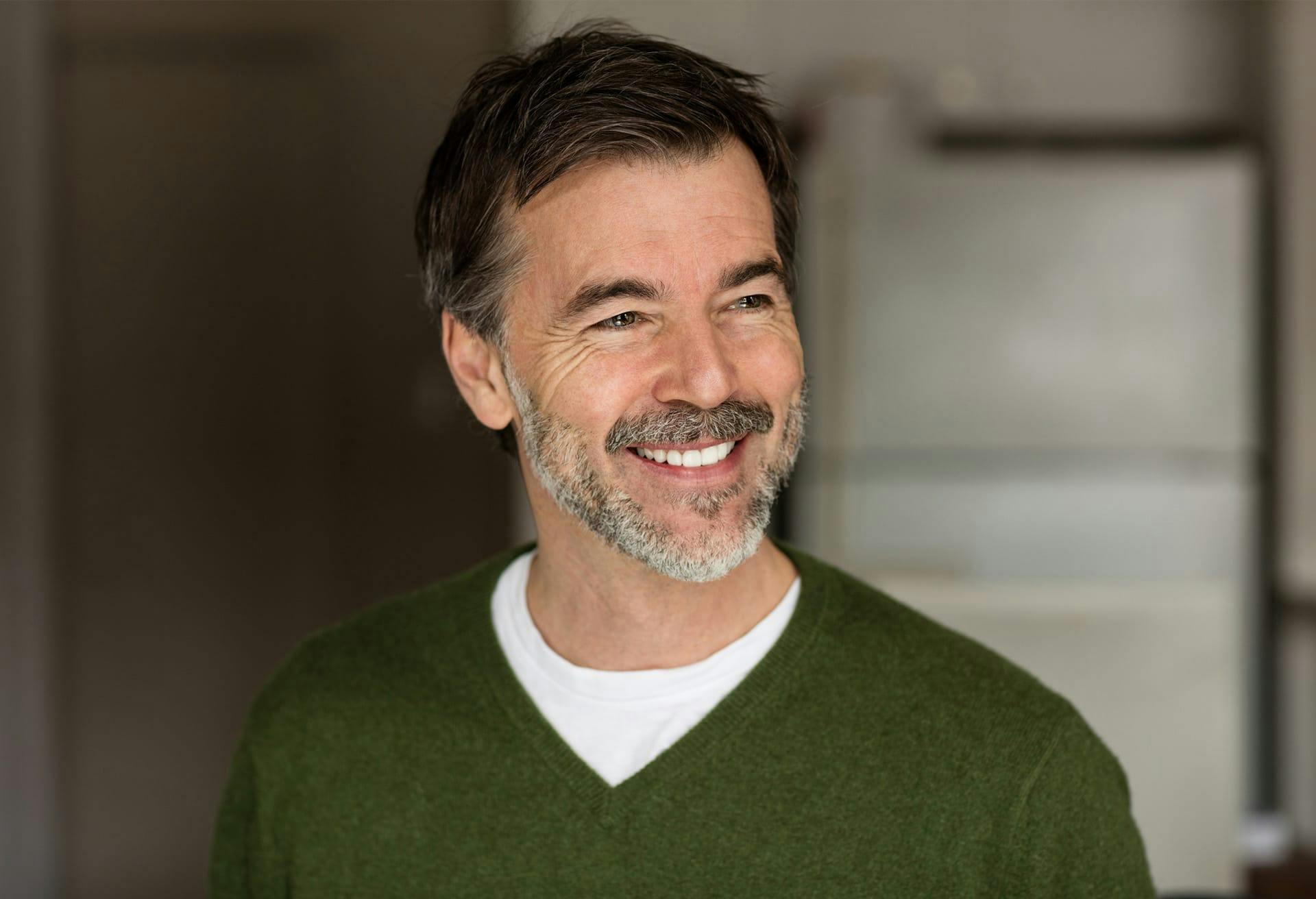 Smiling man in green sweater looking to his left.