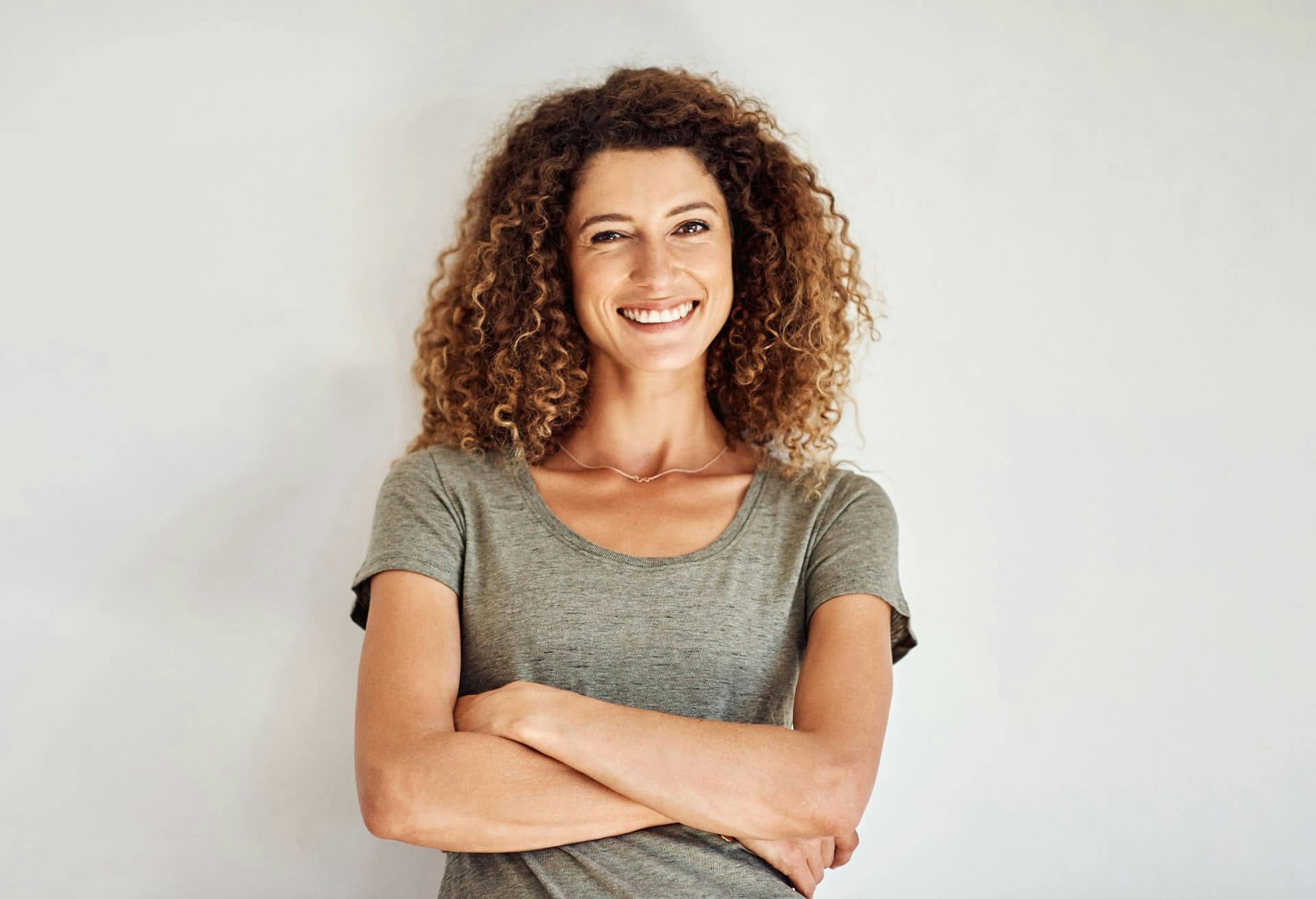 Smiling woman with curly hair crossing her arms.