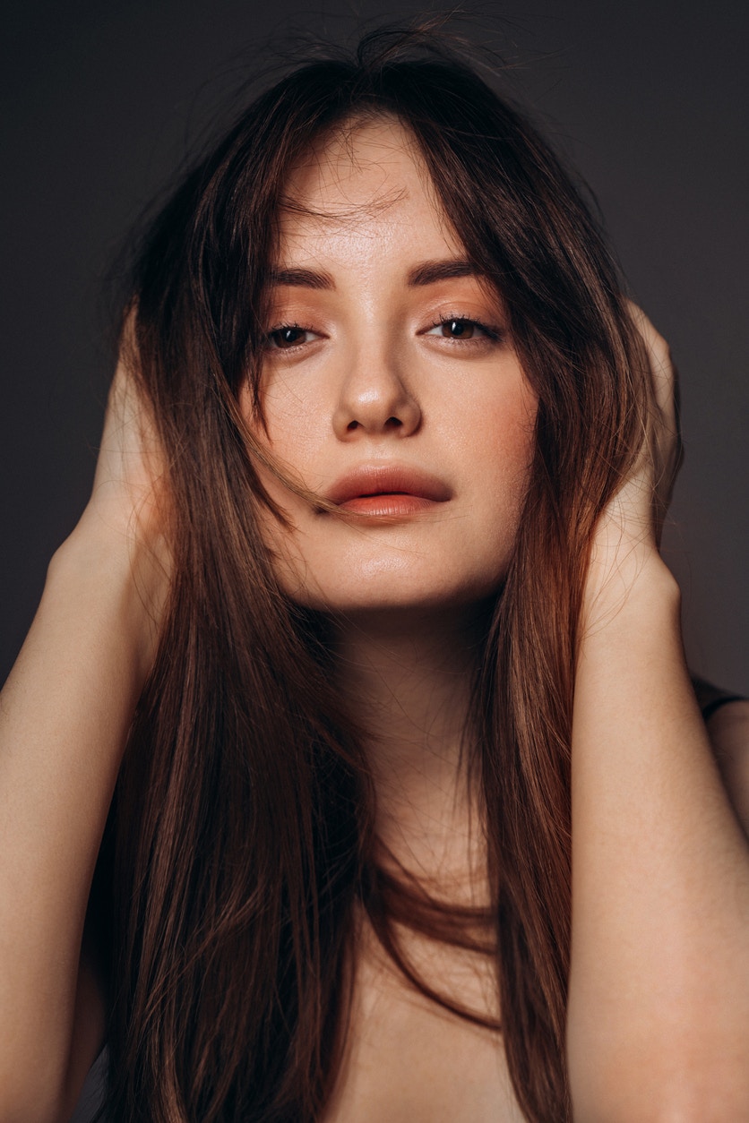 Woman with beautiful smooth skin stares longingly into the camera with hands by head. Her perfect skin emulate the potential results one could achieve with BOTOX in Denver