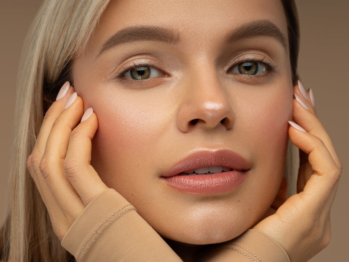 Woman with beautiful skin smiles at the camera with hands on her face in a studio shoot. Her glowing skin represents the potential results of chemical peels in Denver with Denver Facial Plastics