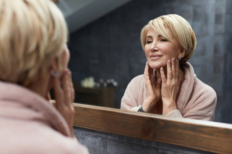 Beautiful older woman looking at face in bathroom