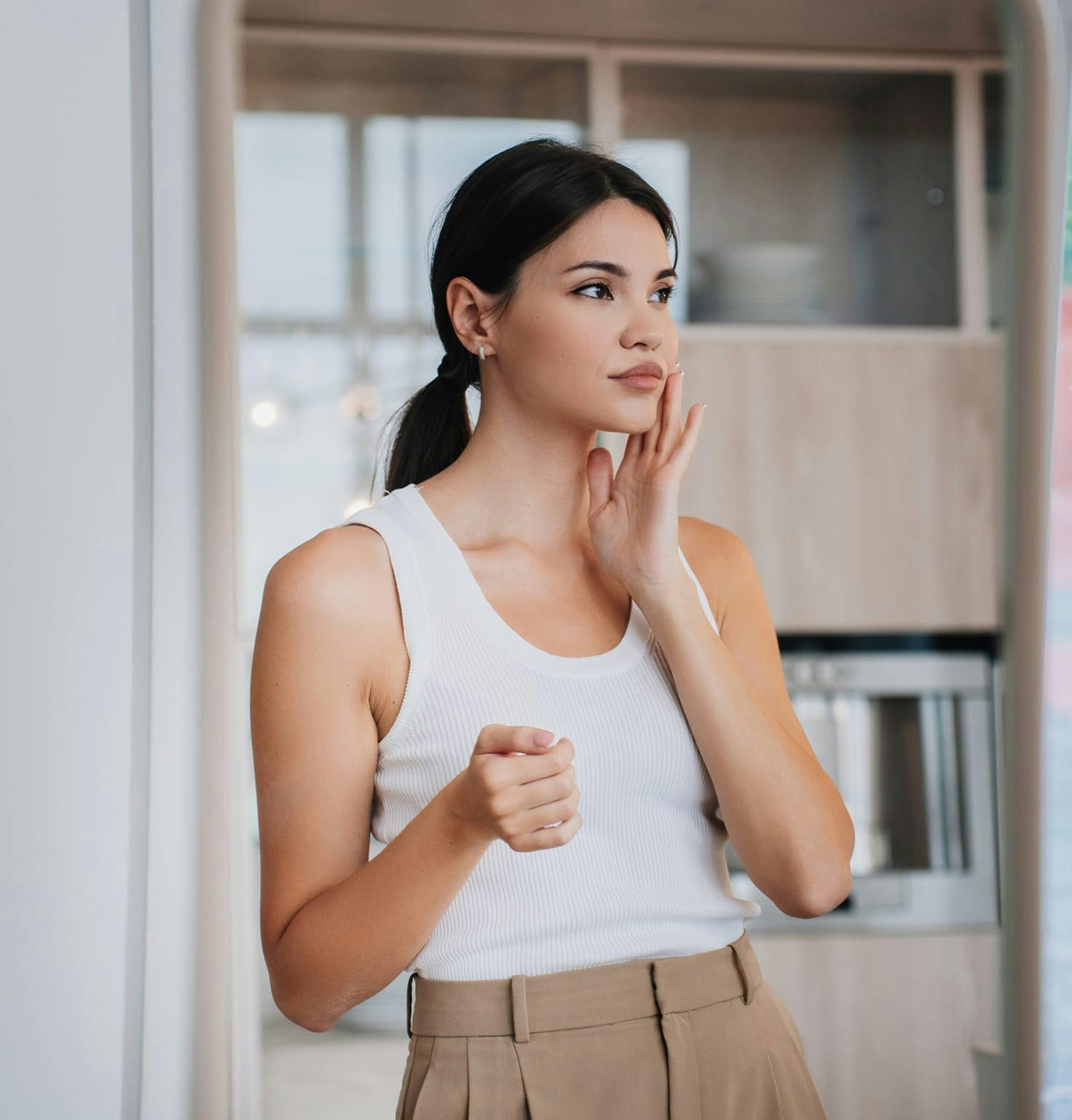 Woman with her dark hair in a ponytail wearing a white top and khaki pants
