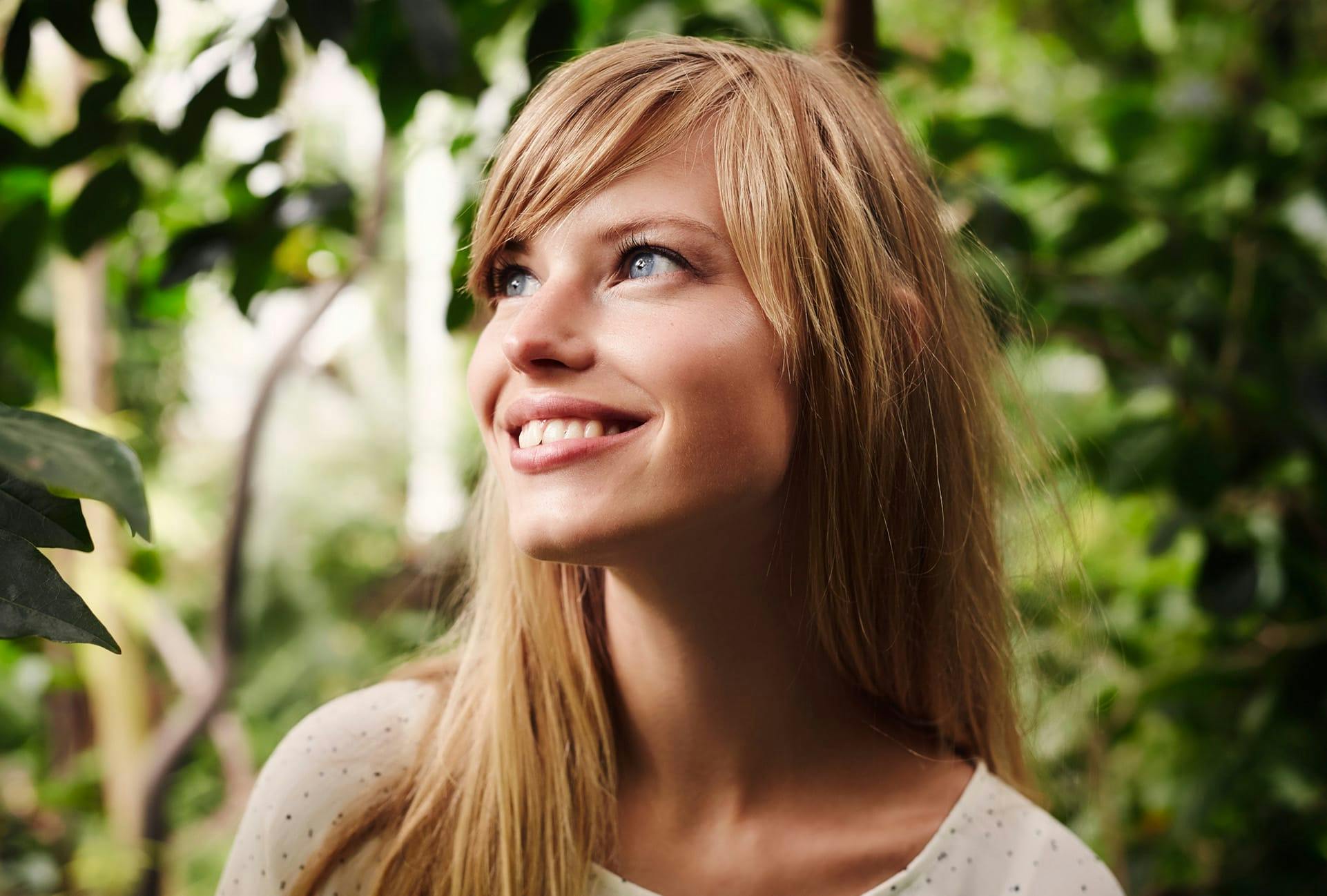 woman smiling with plants and trees behind her