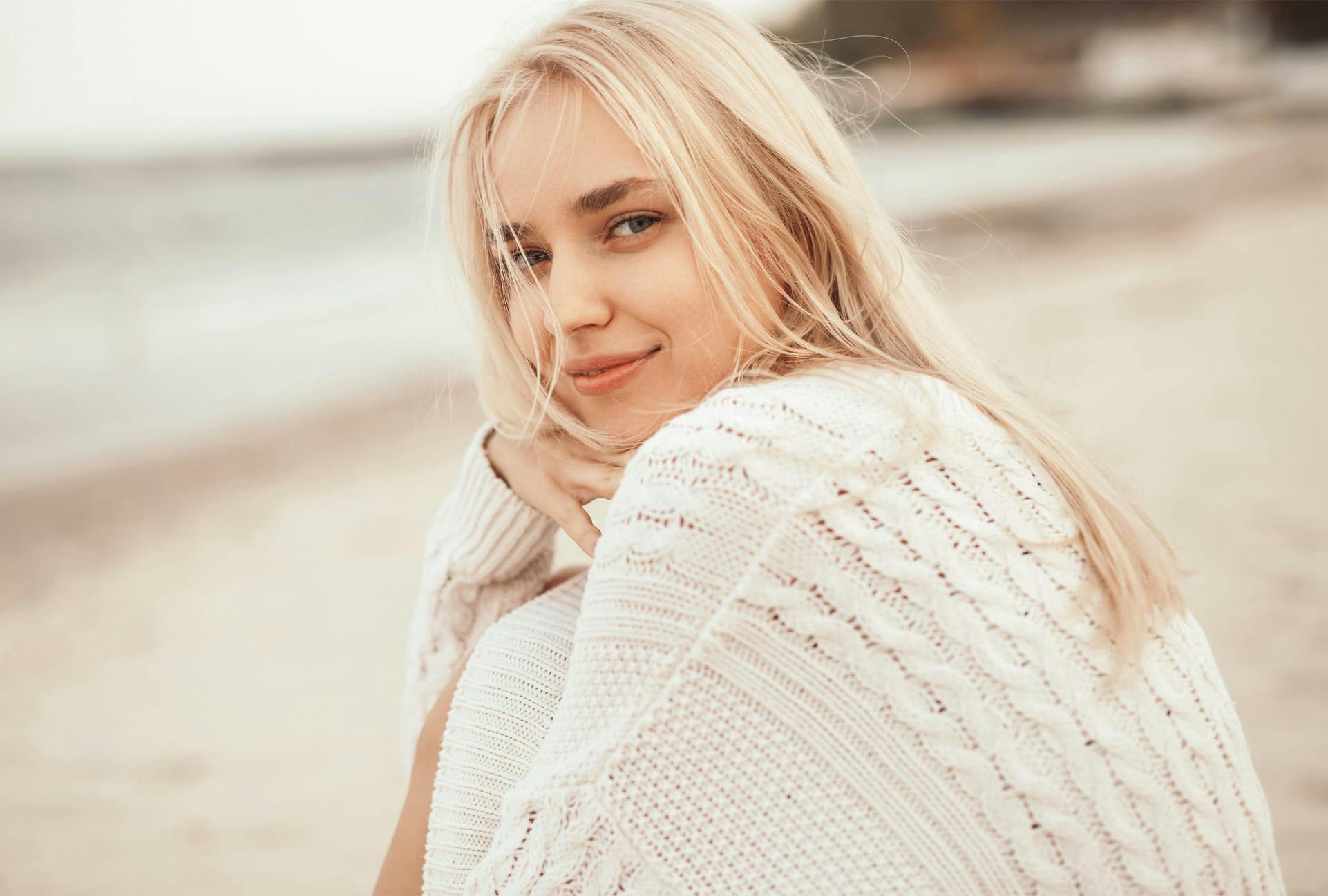 Woman with blonde hair wearing a knit sweater at the beach