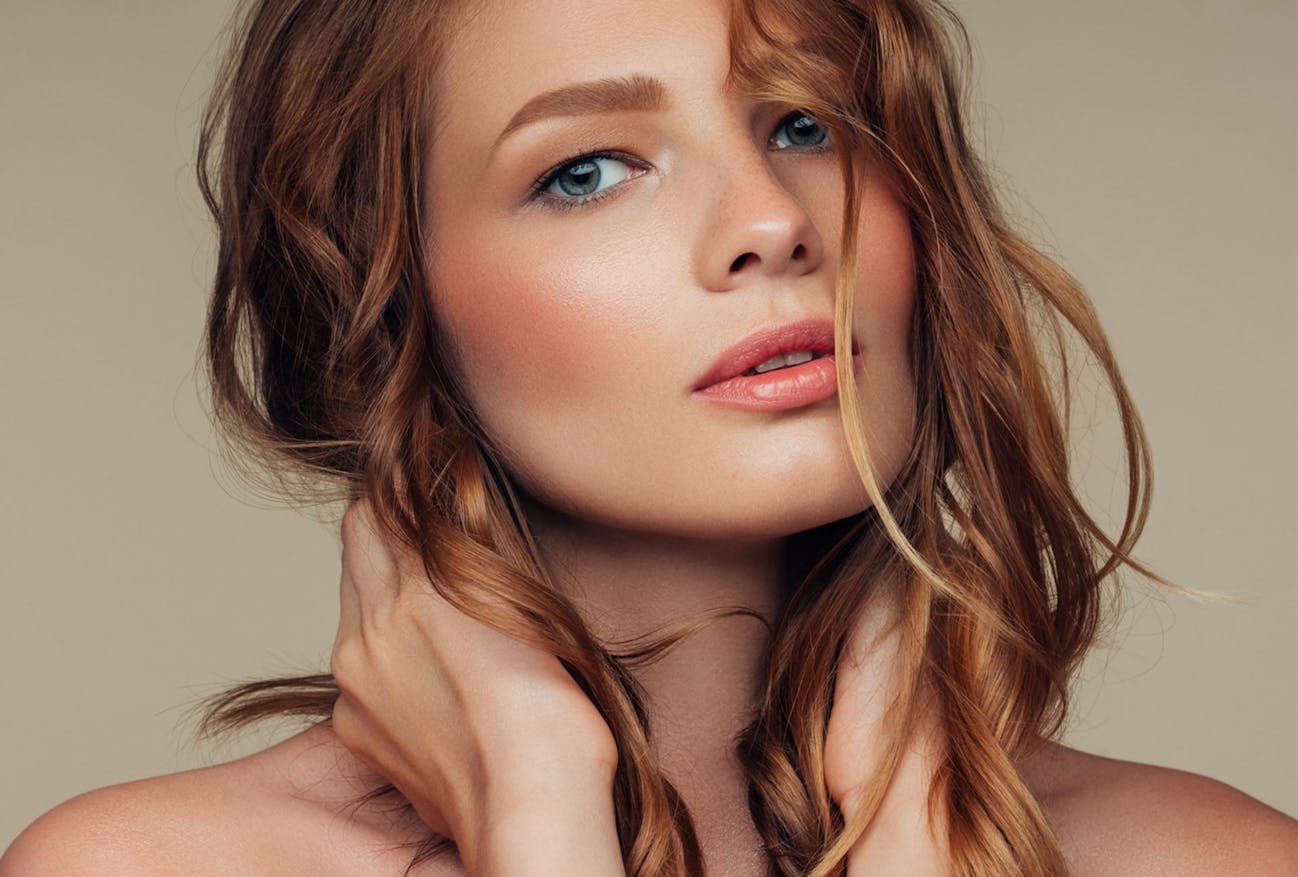 Woman with red hair and both hands to the sides of her neck