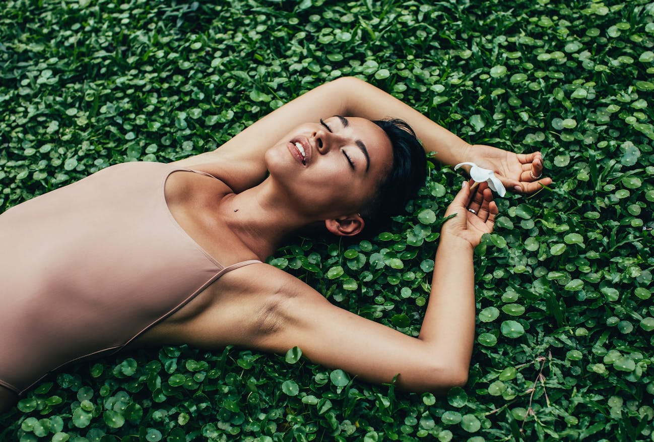 Woman lying down on some plants with her eyes closed