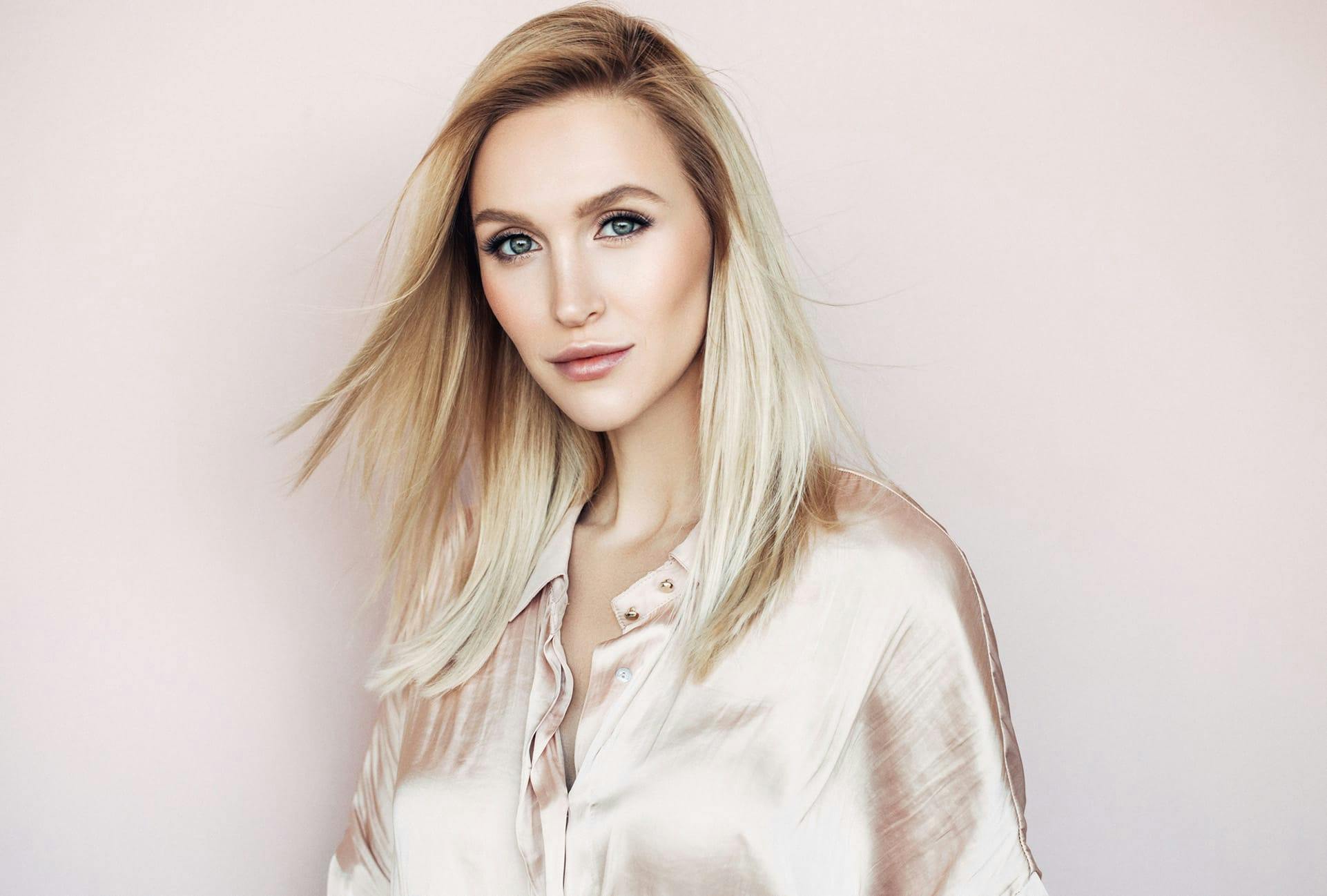 Woman with long blonde hair wearing a light pink satin shirt