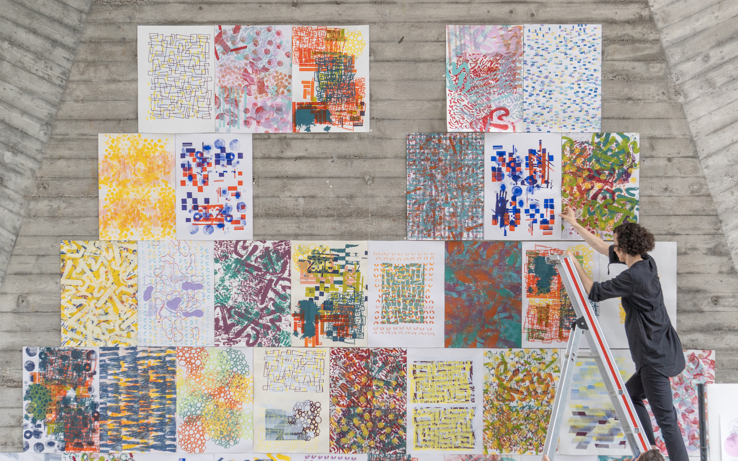 Lehrperson auf Leiter beim Aufhängen von Entwürfen in der Maurerhalle.